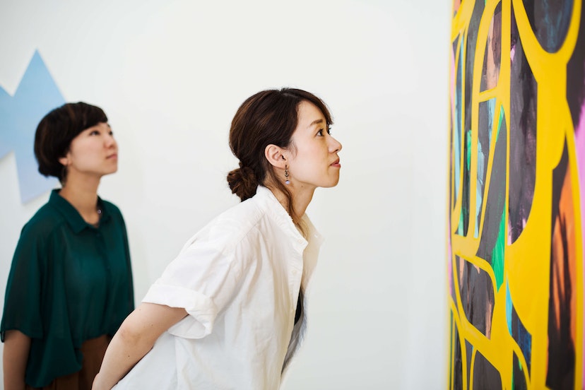 Two women standing in an art gallery, looking at an abstract modern painting. - stock photo