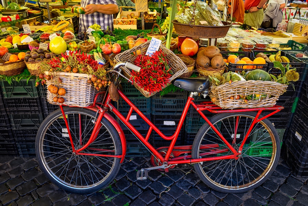Red vintage bike with fresh produce in baskets at a market on Campo di Fiori.