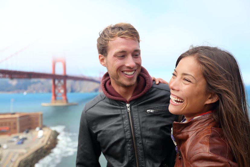 Happy young couple laughing in San Francisco by Golden Gate Bridge. Interracial young modern couple, Asian woman, Caucasian man. 